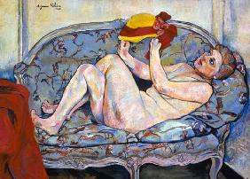 Lying female act on a chaise longue with hat in the hand.