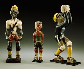 Three Male Carved Figures, One Wearing An Official''s Uniform, The Other Two In Sports Gear